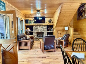 A cozy log cabin interior with a stone fireplace, leather furniture, and a television mounted above it. - Big South Fork! Peaceful, Relaxing, On the Trails…Six Decks ~ Nature’s Paradise! (Strunk)