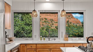A kitchen with wooden cabinets, a white countertop, a sink, and a gas stove. There are two pendant lights hanging above the countertop.