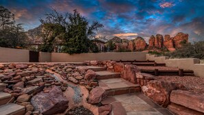A landscaped outdoor area with stone steps and rock formations, surrounded by trees and a mountainous backdrop.