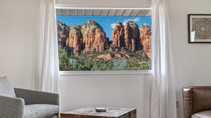 A room with a view of red rock formations through a window, a gray sofa, a wooden coffee table, and a brown leather chair.