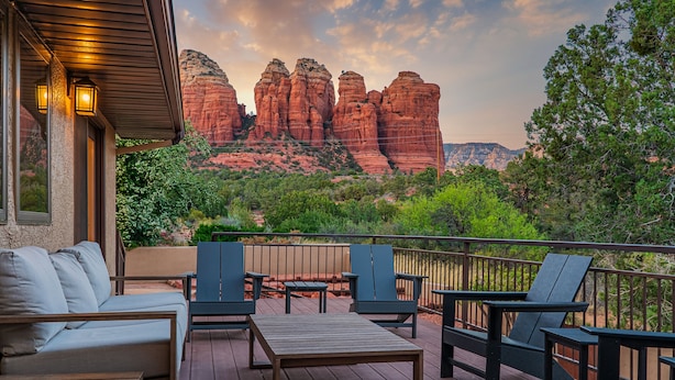 A deck with outdoor furniture, a view of red rock formations, and a wooden deck railing.