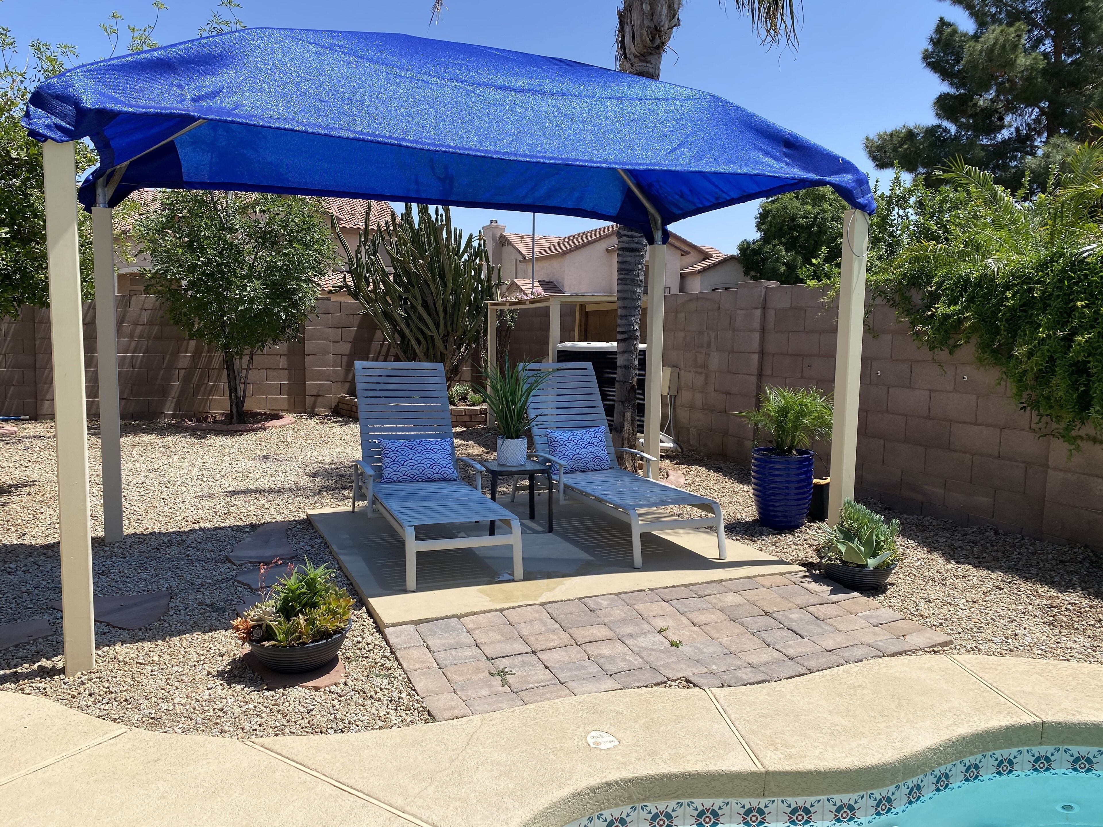 Un patio coperto con due poltrone e un tavolo, immerso in una piscina e in un giardino.