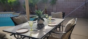 An outdoor patio with a table set for four, surrounded by chairs, a potted plant, and a pool in the background. - Beautiful, 3 bedroom , 2bath ,heated pool , pool table  (Avondale)