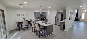 A modern kitchen with a central island, grey cabinets, stainless steel appliances, and a dining area with bar stools. - Beautiful, 3 bedroom , 2bath ,heated pool , pool table  (Avondale)