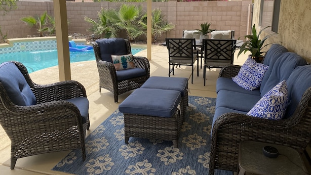Un patio couvert aménagé avec des meubles en osier, une piscine et une vue sur le jardin arrière.
