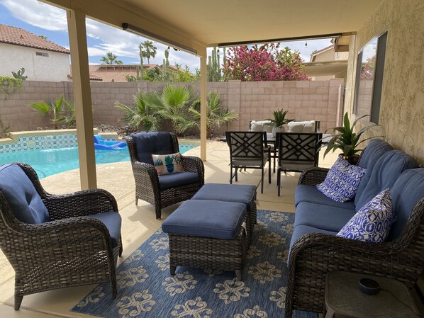 Un patio couvert aménagé avec des meubles en osier, une piscine et une vue sur le jardin arrière.