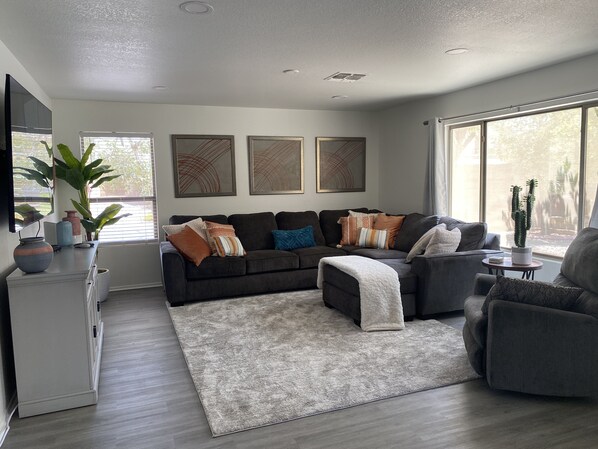 Ein modernes Wohnzimmer mit einem Ecksofa, einem grauen Sessel und einem großen Fenster, das für natürliches Licht sorgt.