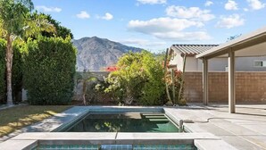 Ein Schwimmbecken mit Bergblick, umgeben von üppiger Vegetation und einer überdachten Terrasse.