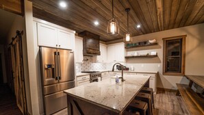 Een moderne keuken met roestvrijstalen apparatuur, een groot eiland met barkrukken, een houten plafond en inbouwplanken.