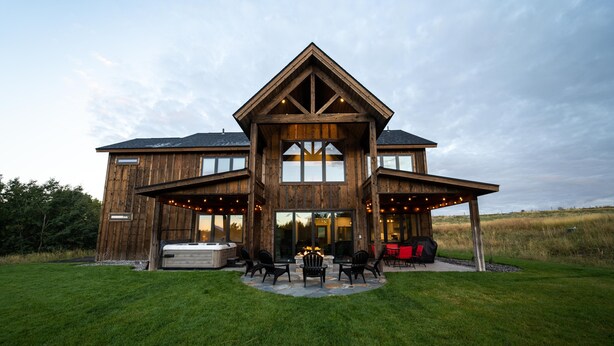 Een groot houten huis met een overdekt terras, buitenmeubels en een jacuzzi.