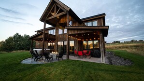 Een groot houten huis met een patio, complete met buiten zitplaatsen en een vuurkuil.