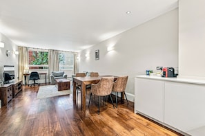A modern kitchen with a dining area, wooden flooring, and a view of greenery outside.