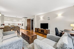 Una sala de estar moderna con un televisor de pantalla plana, una mesa de centro de madera y sofás grises.
