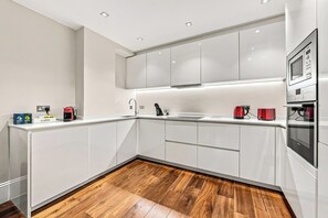 Een moderne keuken met witte kastjes, een houten vloer en ingebouwde apparatuur, waaronder een magnetron en koffiezetapparaat.