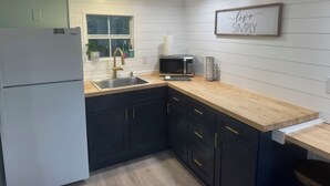 A kitchen with a refrigerator, sink, microwave, and wooden countertop.
