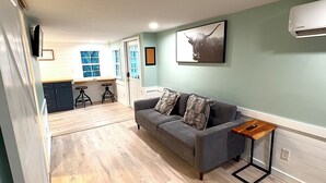 A modern living room with a grey sofa, wooden coffee table, and a kitchen in the background.