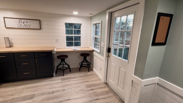 A kitchen with dark cabinets, a wooden countertop, two stools, and a door with windows.