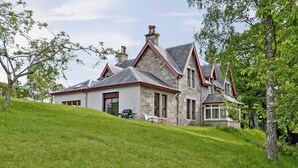 A stone house with a sloped roof and red trim, situated on a grassy hill.