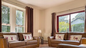 A cozy living room with two brown leather sofas, a patterned rug, and large windows with curtains.
