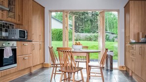 A modern kitchen with wooden cabinets, a built-in microwave, and a dining area with a table and chairs.