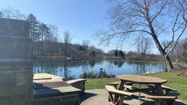 Une terrasse en pierre avec une table de pique-nique en bois et des bancs, le tout donnant sur un lac.