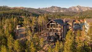 A modern lodge with a large deck and multiple levels, surrounded by dense forest and mountains. - Big Sky Luxury Estate, Mountain Views, 6 Bed 6.5 Bath, Private Lodge, Ski in/out (Big Sky)