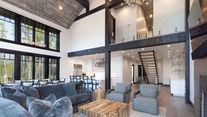 A spacious living area with a high ceiling, large windows, and a modern staircase. - Big Sky Luxury Estate, Mountain Views, 6 Bed 6.5 Bath, Private Lodge, Ski in/out (Big Sky)
