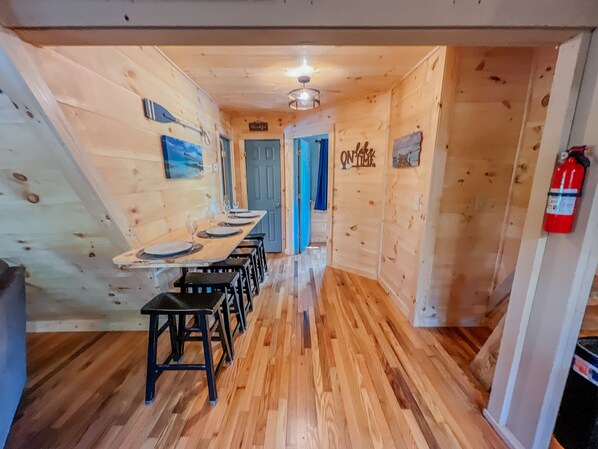 Un interior de madera con una larga mesa de comedor, sillas negras y una puerta azul.