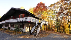 Une cabane à deux étages dotée d’un balcon, d’un escalier et d’une allée bordée du feuillage automnal.