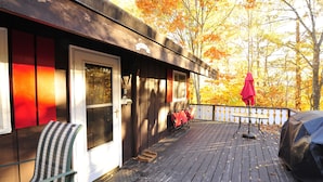 Une terrasse en bois avec un banc, un barbecue couvert et un parasol rouge.