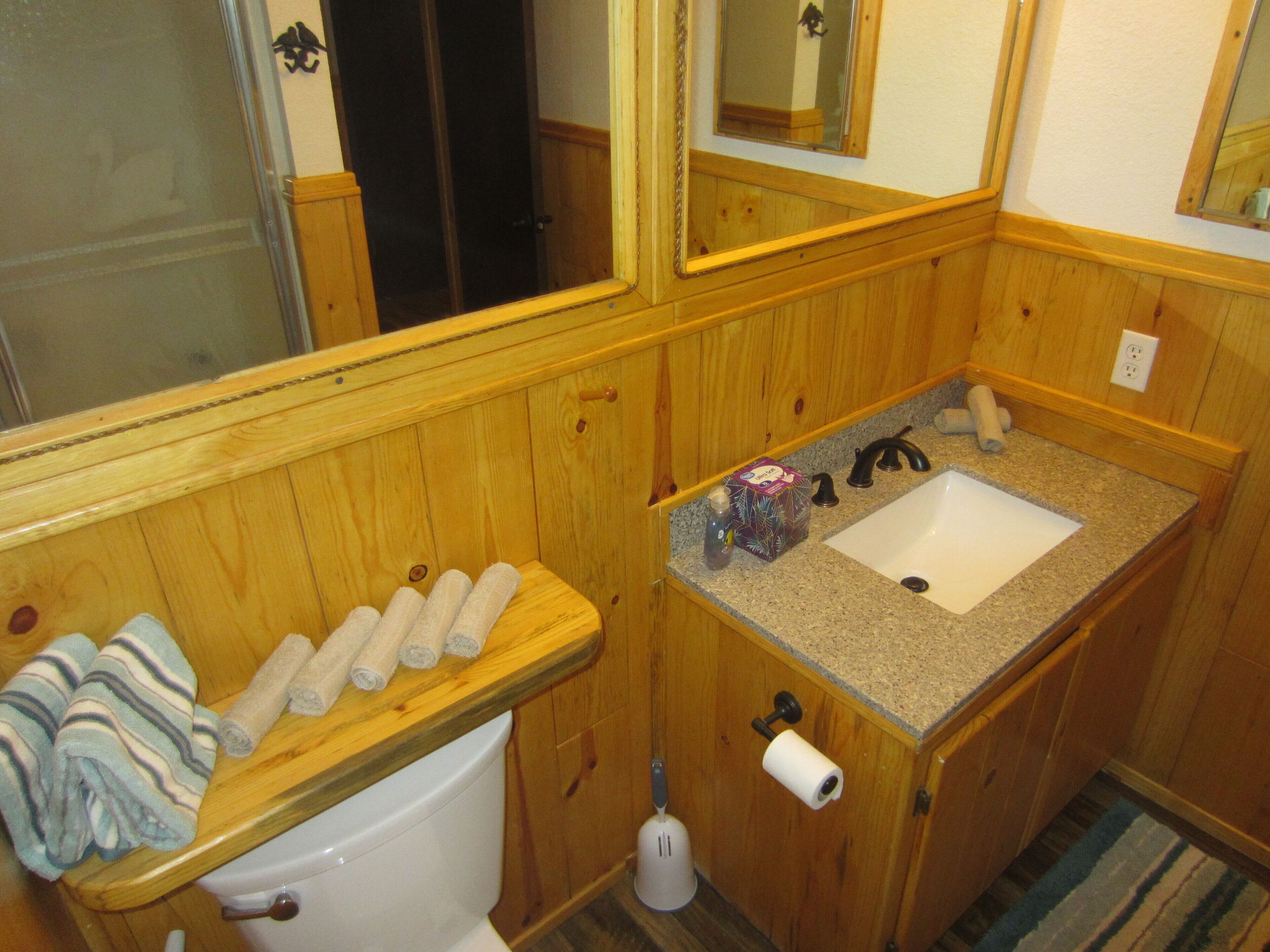 A wooden bathroom with a toilet, sink, and mirror.