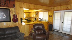 A wooden interior with a leather sofa, a leather armchair, a kitchen area, and a dining table.