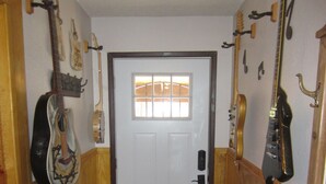 A narrow hallway with wooden walls, a white door with a window, and guitars hanging on the walls.