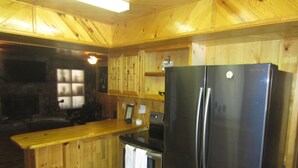 A kitchen with wooden cabinets, a stainless steel refrigerator, and a stone fireplace.