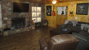 A cozy living room with a stone fireplace, leather sofa, and wooden walls.