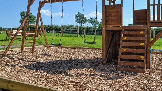 Une aire de jeux en bois avec des balançoires, un toboggan et une structure d’escalade.