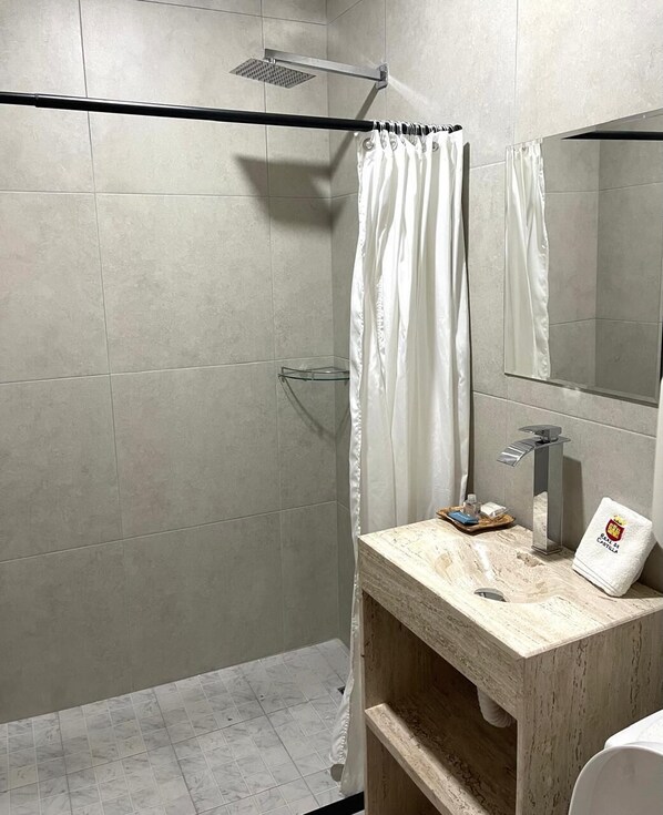 Un baño moderno con ducha, repisa de vidrio, tocador de madera y espejo.