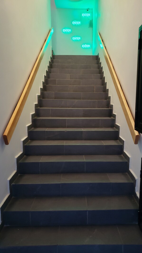 Un escalier aux marches sombres et aux rampes en bois, menant à une porte sur laquelle on peut lire les mots « ENTRÉE ».