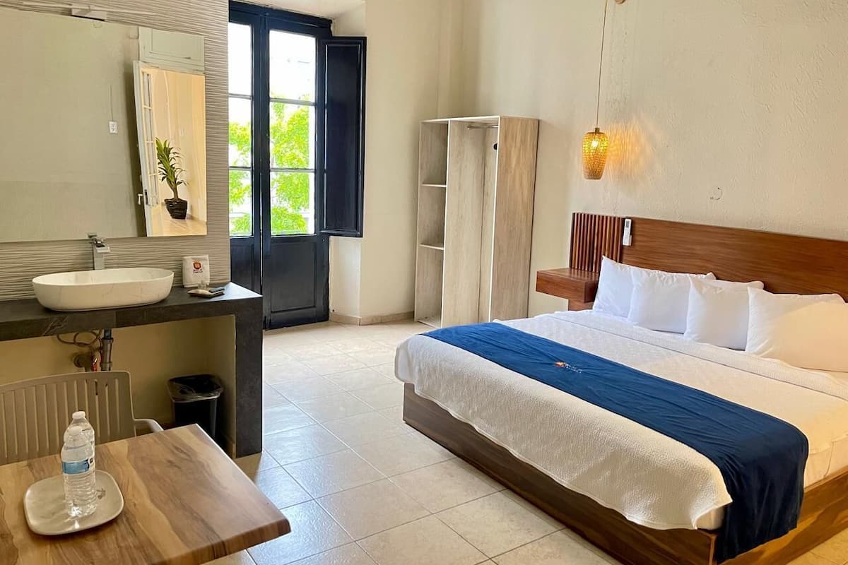 A hotel room with a bed, a bedside table, a sink, and a mirror.