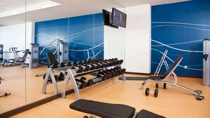 Un gimnasio con equipo de levantamiento de pesas, un televisor y un espejo.