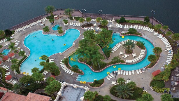 Vista aérea de un resort con varias piscinas, tumbonas y palmeras.