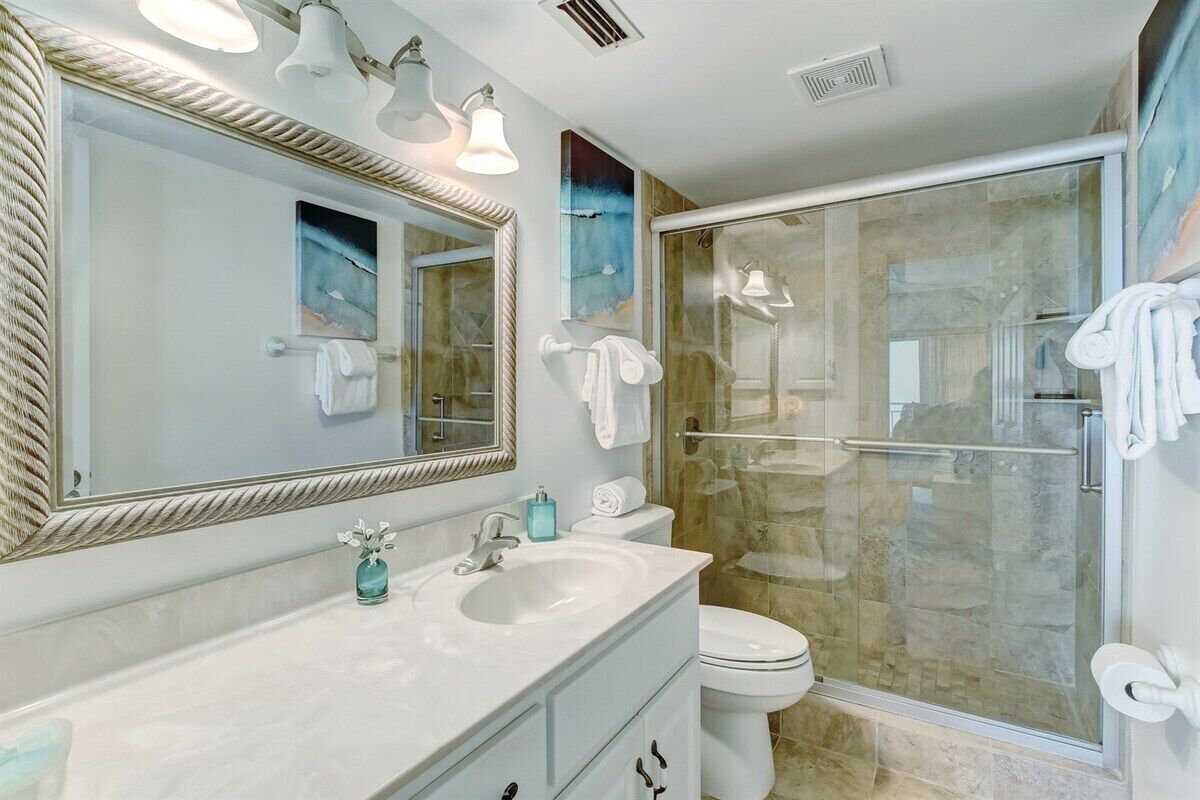 Une salle de bain moderne avec un grand miroir, un lavabo, des toilettes et une douche à parois de verre.