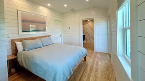 A bedroom with a bed, wooden flooring, a window, and a painting on the wall.