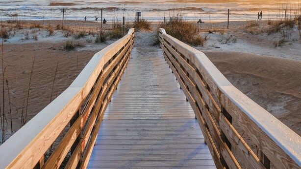 A wooden boardwalk leading to a beach with a clear sky.