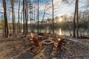 A campsite with wooden chairs and a fire pit surrounded by trees and a lake.