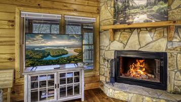 A cozy room with a stone fireplace, a large TV mounted on a wooden cabinet, and a scenic painting above the fireplace.