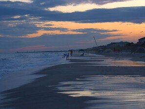 Ein Strand bei Sonnenuntergang, Menschen spazieren und fischen.