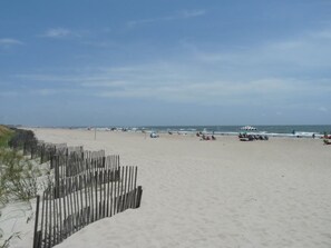A wide sandy beach with a wooden fence on one side and a few beach umbrellas and chairs. - 2708 Commons II (Calabash)