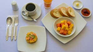 Ein Frühstückstisch mit einer Schale gewürfeltem Obst, einem Muffin, Toast, einer Tasse Kaffee, einem Glas Orangensaft und einer kleinen Schale Marmelade.
