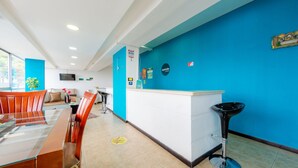 Eine moderne Hotelhalle mit einer Rezeption, einer Sitzecke mit Glastisch und Stühlen sowie einer blauen Akzentwand.